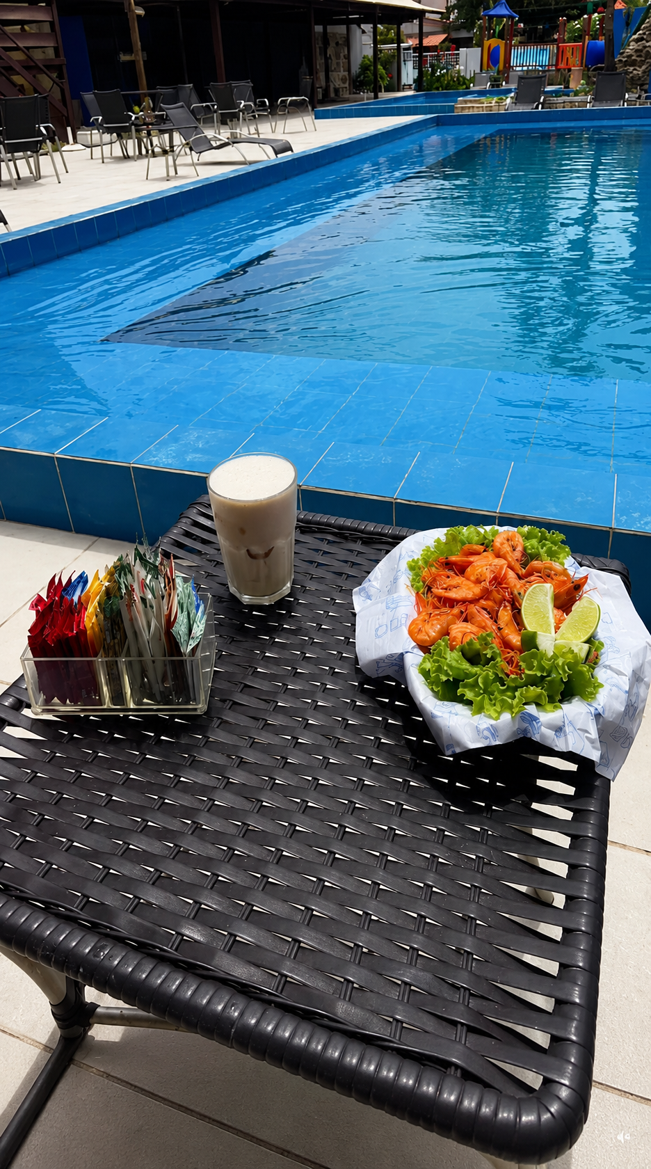 Porção de camarão e bebida na mesa junto à piscina