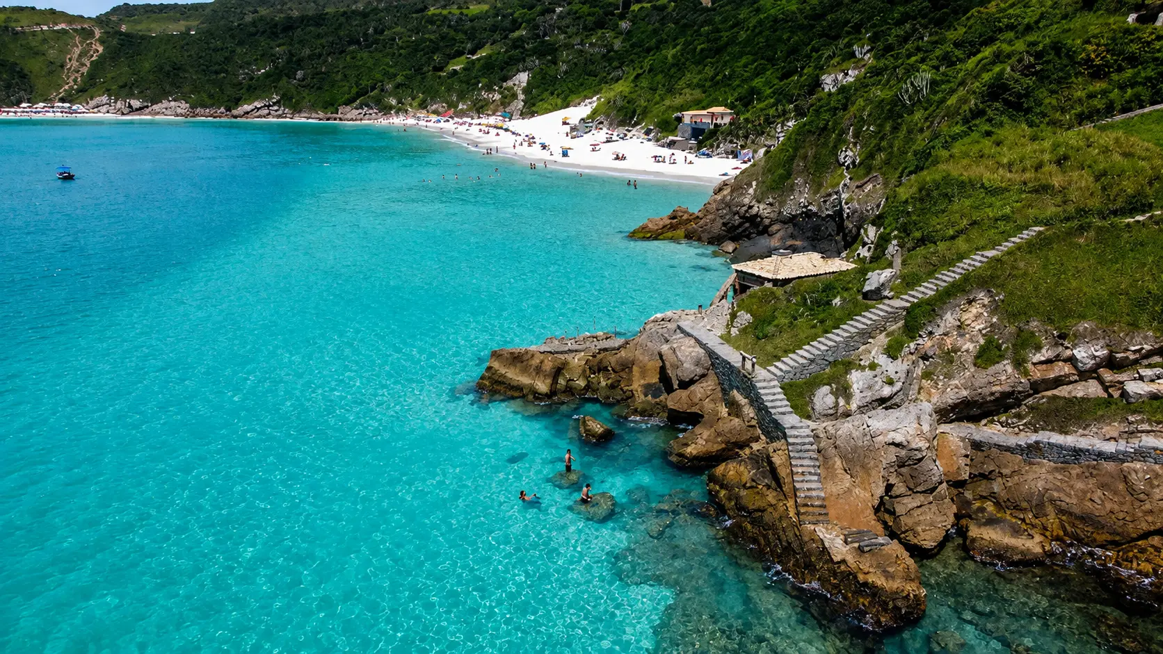 Escada de pedra sobre as rochas com vista para a areia branca das Prainhas