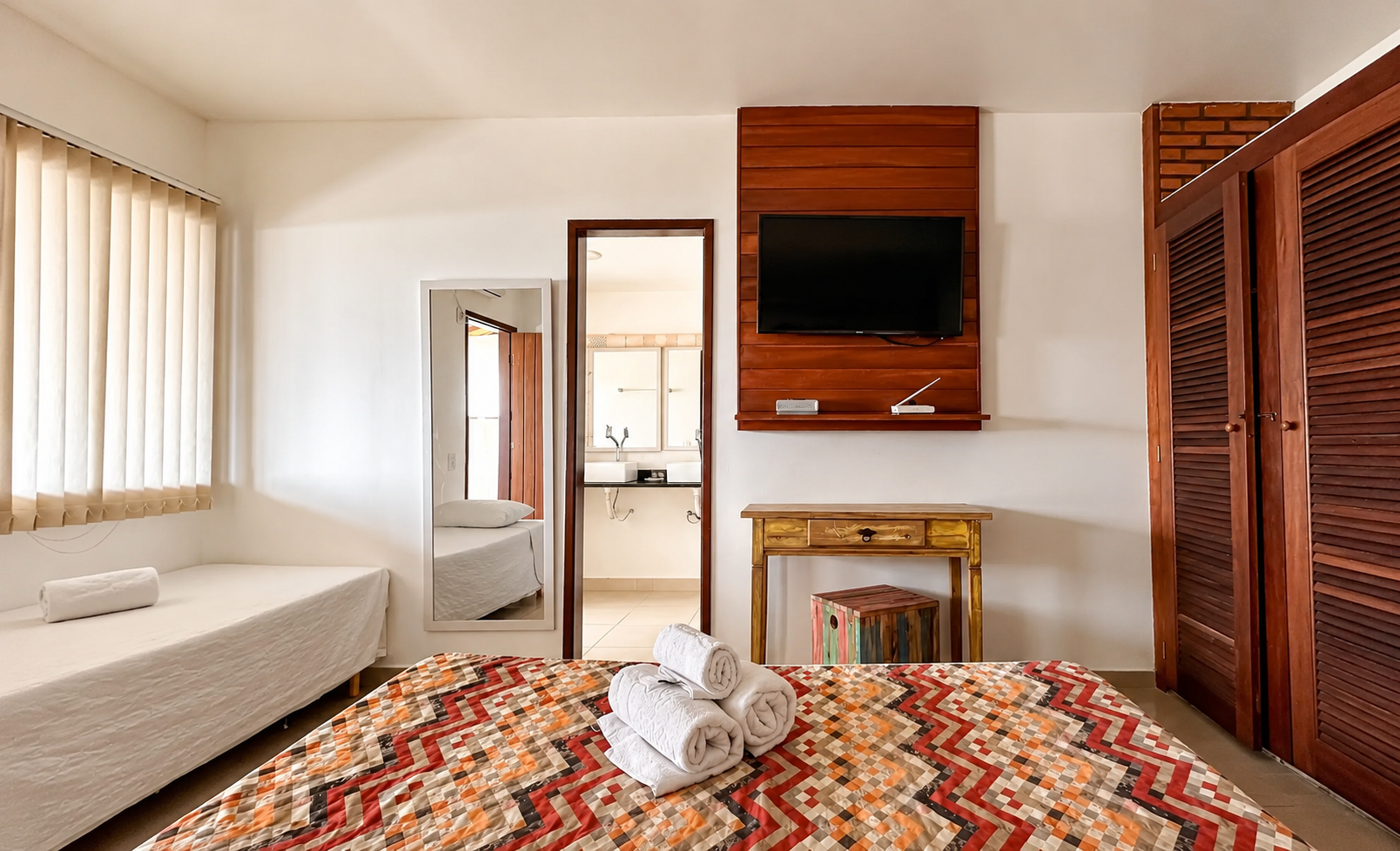 Interior do quarto com TV, armário de madeira e cama de solteiro extra